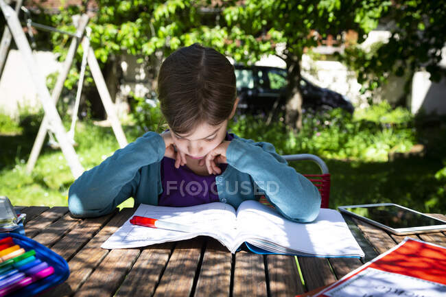 Mädchen sitzt am Gartentisch und macht Hausaufgaben — Stockfoto
