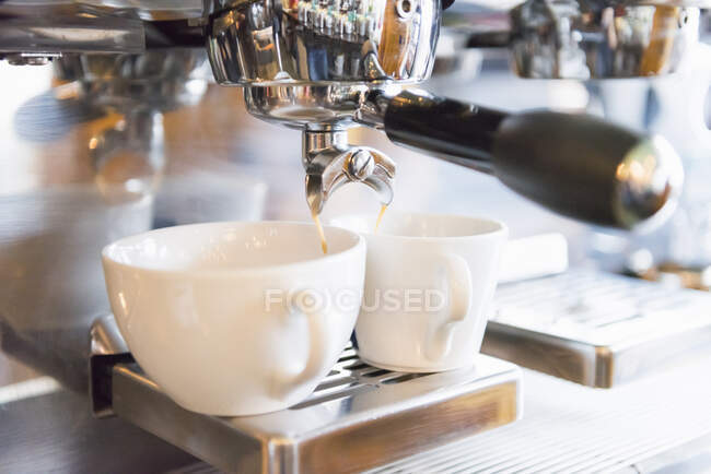 Primer plano del café que se vierte en la taza de la cafetera espresso en la tienda - foto de stock