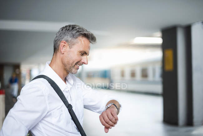 Uomo d'affari tempo di controllo mentre seduto alla stazione ferroviaria piattaforma — Foto stock