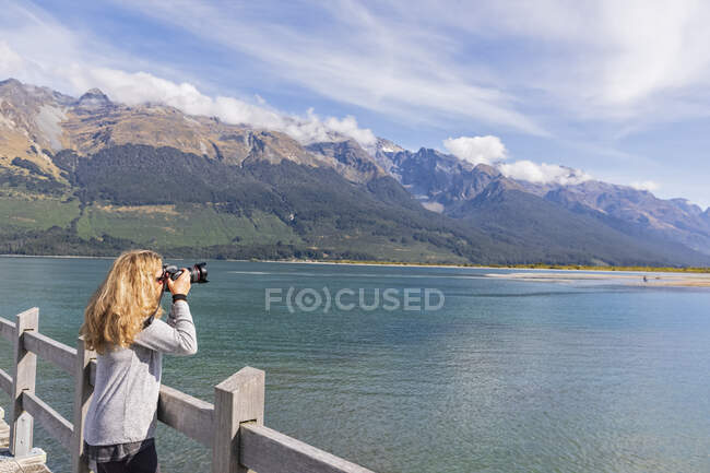 Nuova Zelanda, Oceania, Isola del Sud, Otago, Lago Wakatipu, Alpi neozelandesi, Glenorchy, Donna che fotografa il paesaggio dal molo — Foto stock
