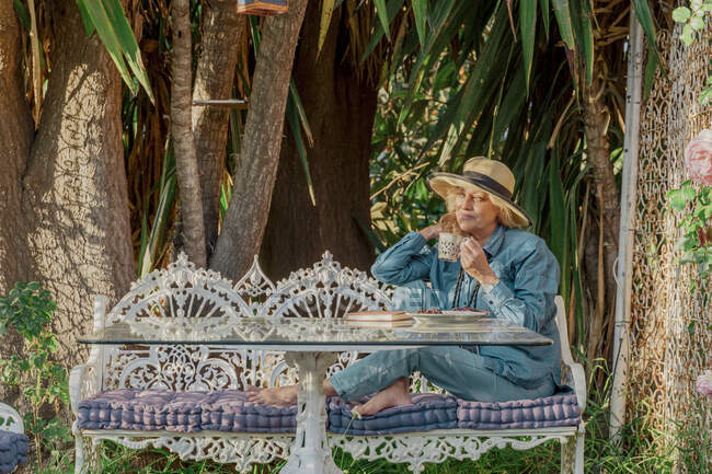 Seniorin sitzt auf Gartenbank und trinkt Tee — Stockfoto