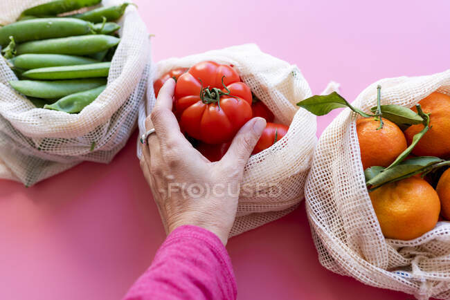 Рука жінки, яка збирає свіжий помідор з екологічно чистої багаторазової сітки — стокове фото