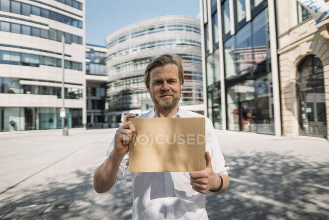 Retrato del hombre sonriente sosteniendo cartón en blanco en la ciudad - foto de stock