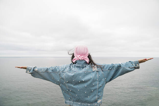 Молода жінка, яка перенесла рак, з розтягнутими руками дивиться на море проти хмарного неба. — стокове фото