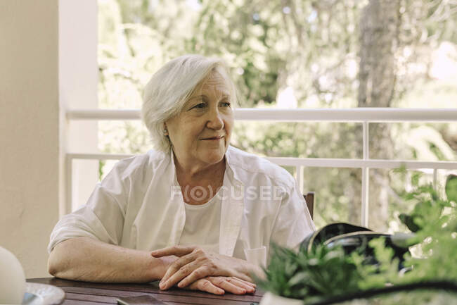 Femme âgée réfléchie regardant loin tout en étant assis à la table dans le balcon — Photo de stock
