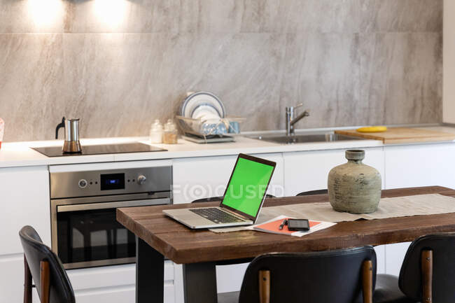 Ноутбук і смартфон на обідньому столі в сучасній кухні вдома — стокове фото
