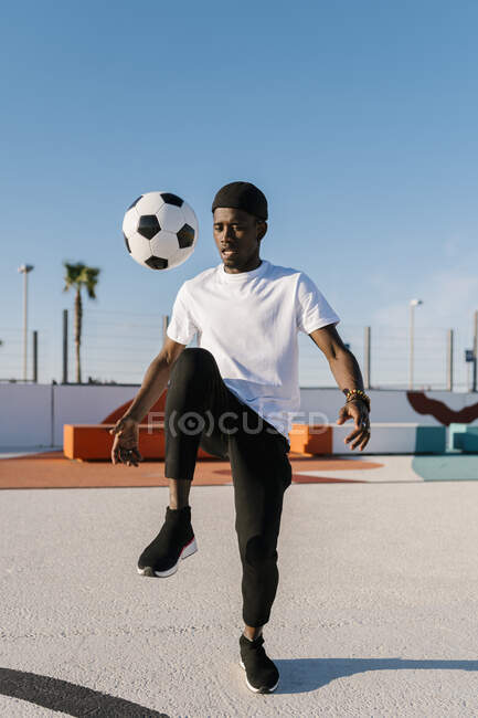 Молодой человек жонглирует футбольным мячом на фоне ясного неба в суде — стоковое фото