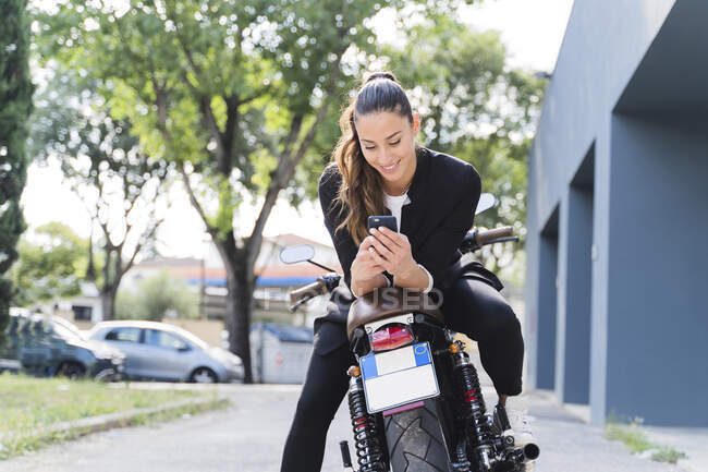 Smiling woman sitting on motorbike and using smartphone — Stock Photo