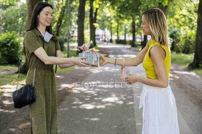 Woman with taken off face mask handing over gift to friend in  nature — Stock Photo