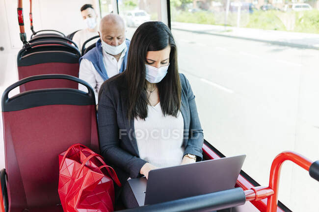 Femme portant un masque de protection dans un bus public utilisant un ordinateur portable, Espagne — Photo de stock