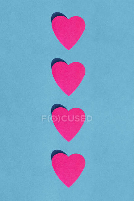 Studio colpo di fila di cuori di carta rosa contro sfondo blu — Foto stock