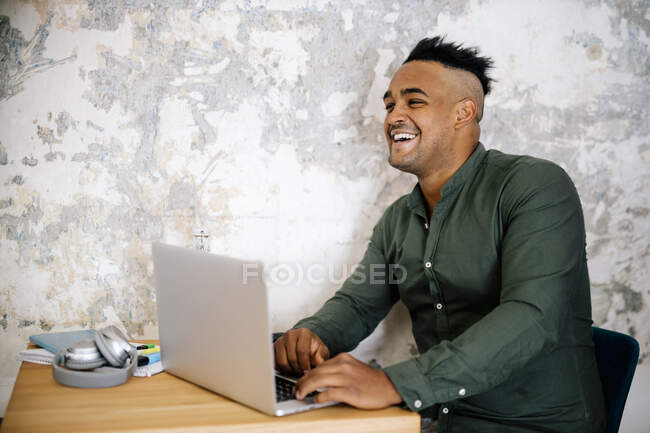 Porträt eines lachenden jungen Mannes, der im Home Office am Laptop arbeitet — Stockfoto