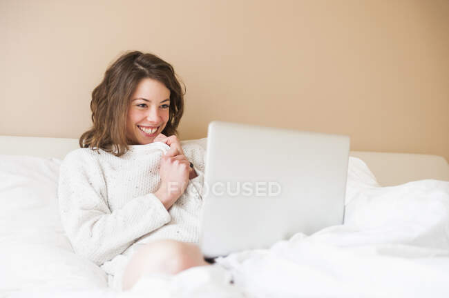 Heureuse jeune femme utilisant un ordinateur portable au lit à la maison — Photo de stock