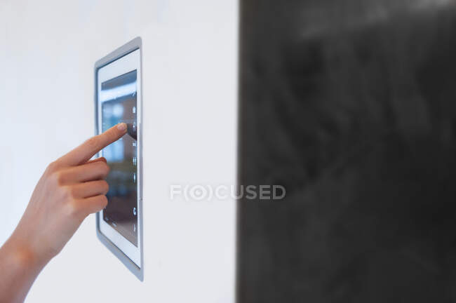 Mano de mujer usando control digital del rayo montado en la pared en casa - foto de stock