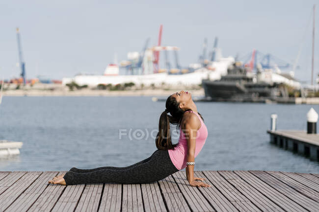 Donna che pratica cobra posa sul molo contro il mare al porto — Foto stock