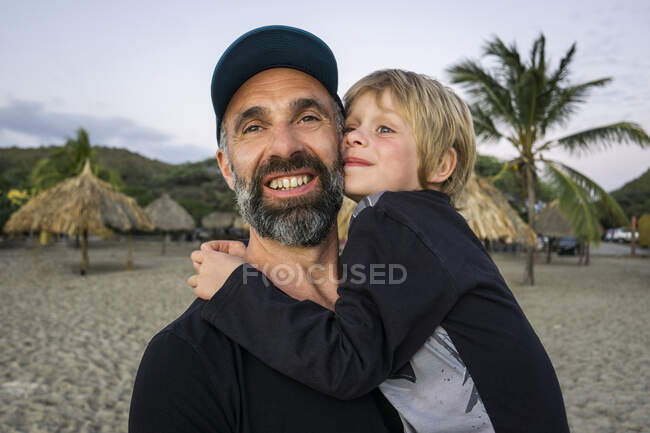 Bearded mature man carrying son while standing at beach — Stock Photo