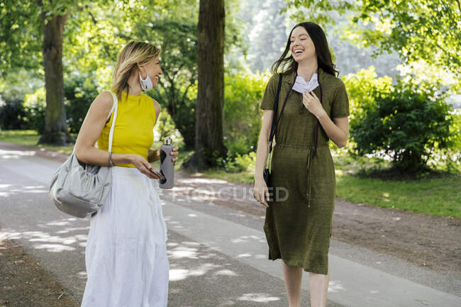 Two happy women meeting in nature while wearing let down face masks — Stock Photo