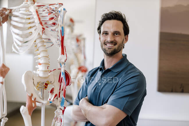 Фізіотерапевт стоїть на анатомічному скелеті з схрещеними руками — стокове фото