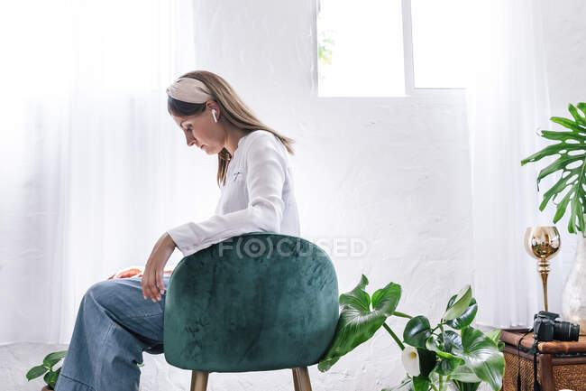 Жінка з довгим каштановим волоссям сидить на стільці у спальні. — стокове фото