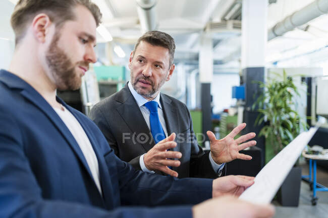 Zwei Geschäftsleute bei einem Arbeitstreffen in einer Fabrik, bei dem ein Plan diskutiert wird — Stockfoto