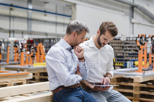Dos hombres compartiendo la tableta en el piso de fábrica - foto de stock