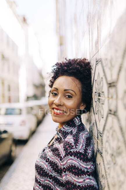 Sorrindo mulher elegante inclinando-se na parede de azulejos na cidade — Fotografia de Stock