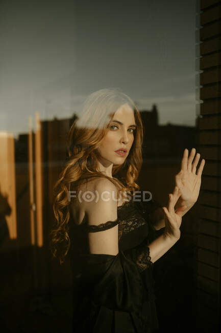 Retrato de una hermosa mujer rubia en lencería negra detrás del cristal de la ventana - foto de stock
