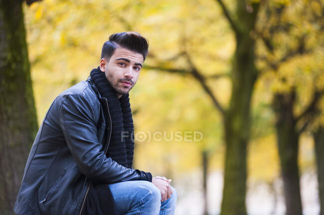 Schöner junger Mann sitzt im Herbst im Park — Stockfoto