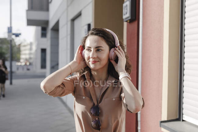 Задумчивая деловая женщина слушает музыку через наушники в солнечный день — стоковое фото