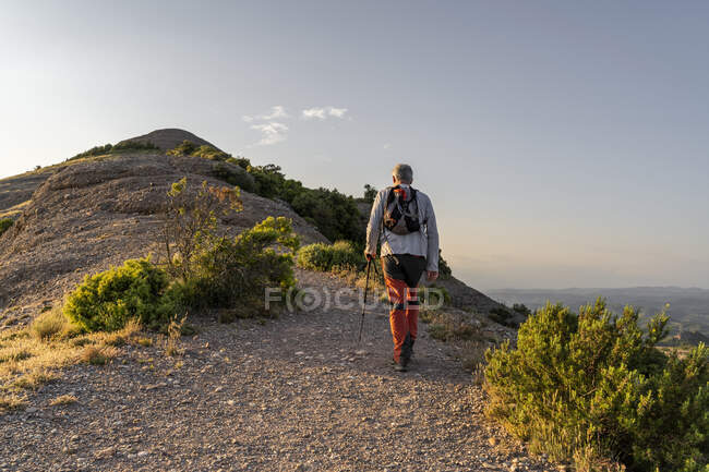 Активний літній чоловік, який під час заходу сонця ходить з полем для прогулянок. — стокове фото