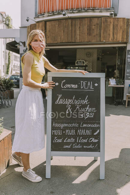 Cafe owner wearing face mask posting a board with Corona special offers — Stock Photo