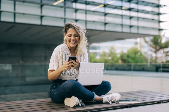 Businesswoman laughing while using mobile phone and laptop outdoors — Stock Photo