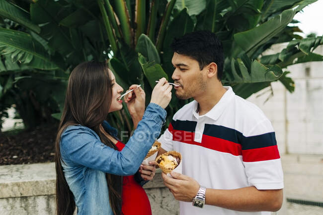 Expectant couple feeding ice creams to each other during sunny day — Stock Photo