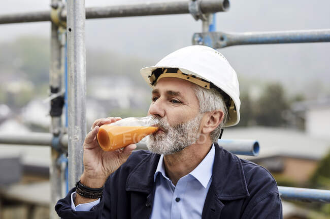 Architect drinking juice on scaffolding on a construction site — Stock Photo