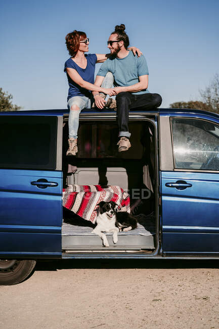 Casal feliz sentado no telhado de uma minivan — Fotografia de Stock