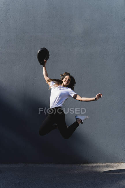 Mulher com capacete de motocicleta pulando na frente da parede cinza — Fotografia de Stock