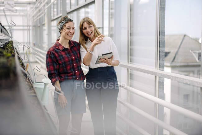 Happy gardener and businesswoman with tablet in greenhouse of a gardening shop — Stock Photo