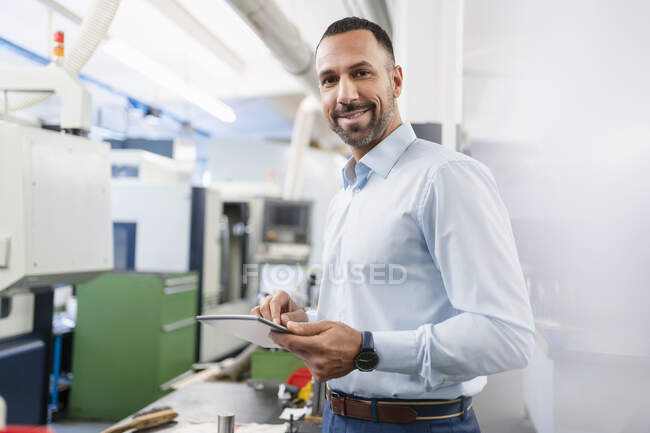 Портрет усміхненого бізнесмена, який тримає планшет у фабричному залі. — стокове фото