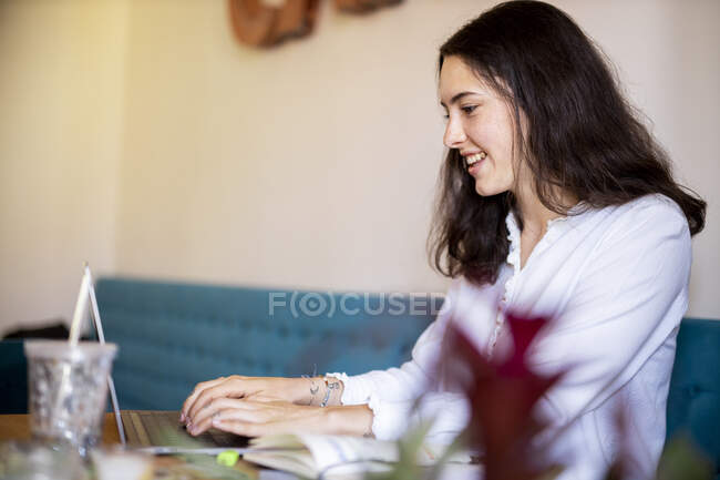 Улыбающаяся молодая женщина, работающая на ноутбуке в домашнем офисе — стоковое фото