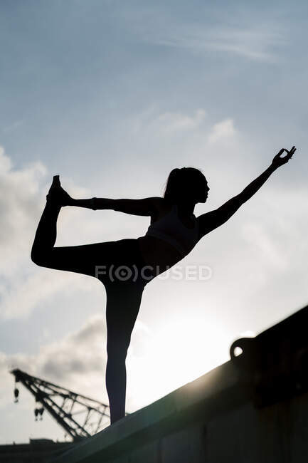 Silhouette atleta femminile pratica Natarajasana sul molo contro il cielo — Foto stock