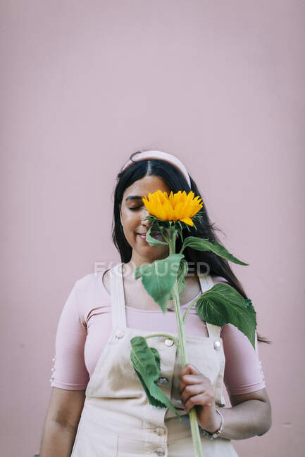 Jeune femme devant le mur rose, oeil couverture avec tournesol — Photo de stock