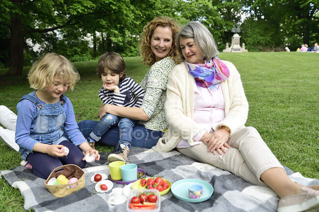 Happy children enjoying picnic with mother and grandmother at public park — Stock Photo