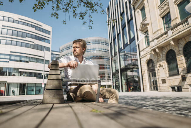 Бізнесмен сидить на лавці в місті за допомогою ноутбука. — стокове фото