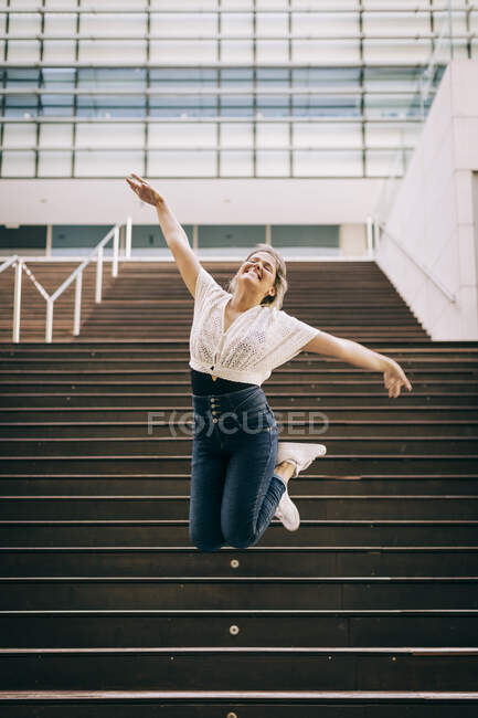 Jovem com braços estendidos pulando em escadaria na cidade — Fotografia de Stock