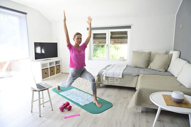 Donna matura con computer portatile che pratica yoga sul tappeto palestra in soggiorno — Foto stock