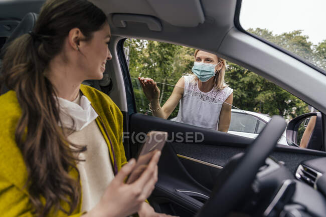 Mujer con una máscara protectora hablando a través de la ventana del coche con la mujer sin máscara — Stock Photo