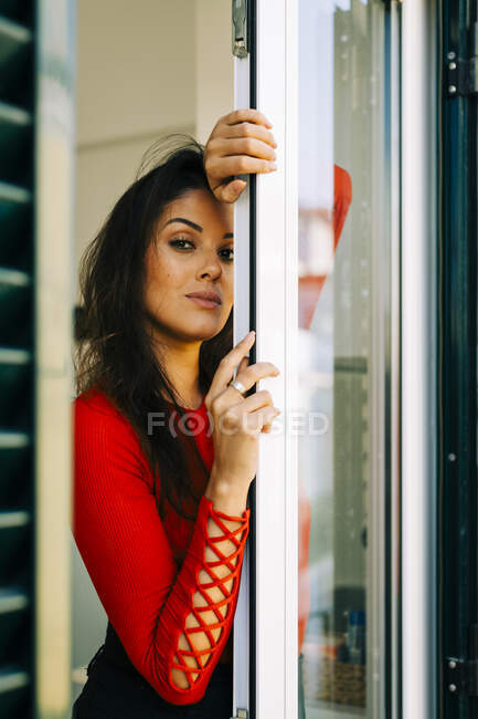Mujer joven seria con el pelo largo de pie por la puerta en casa - foto de stock