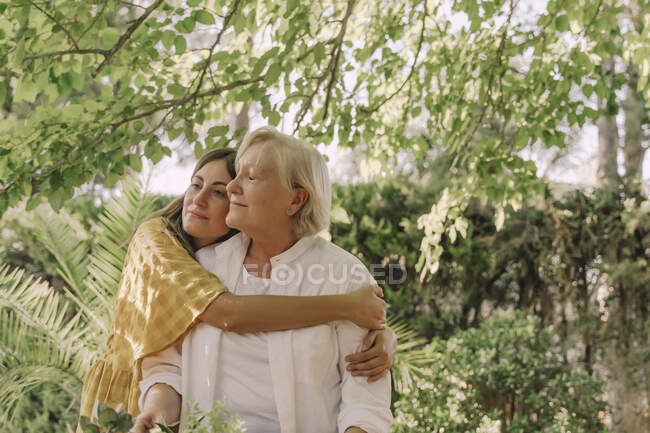 Liebevolle Tochter umarmt Mutter, während sie im Hof gegen Pflanzen steht — Stockfoto