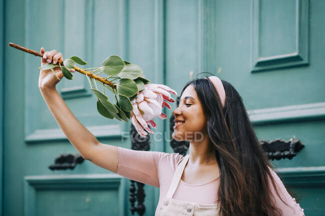 Lächelnde Frau riecht Protea-Blume vor grüner Tür — Stockfoto
