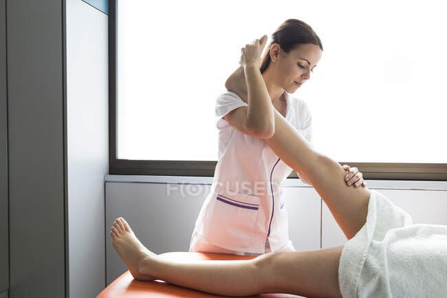 Physiothérapeute féminine étirant la jambe de la patiente — Photo de stock